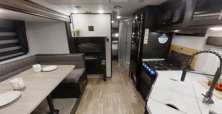 Bright RV rental interior with a dinette, fully-equipped kitchen, and a glimpse of the bedroom and bathroom at the rear.. Forest River Cherokee Grey Wolf 2022