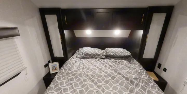 Cozy RV rental bedroom with a full bed, overhead storage, and built-in lighting. Textured walls and modern dark cabinetry create a comfortable space.. Forest River Cherokee Grey Wolf 2022