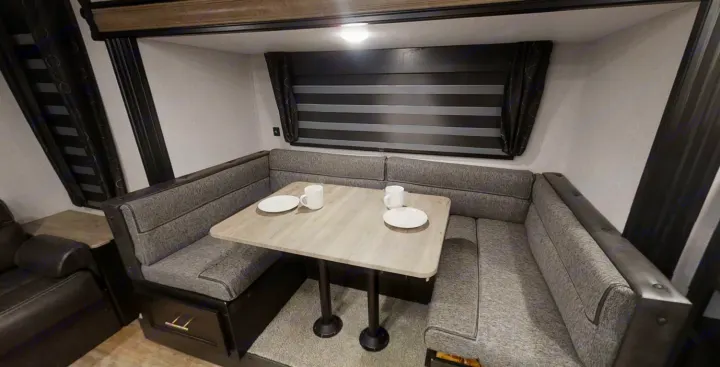 RV rental dinette: U-shaped gray bench seating, light wood table with place settings. Modern interior for comfortable meals & travel.. Forest River Cherokee Grey Wolf 2022