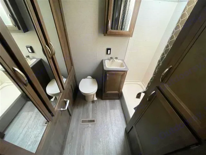 RV rental's compact bathroom features a toilet, vanity sink, standing shower with curtain, and mirrored wardrobe for storage.. Coleman 2305QB 2018