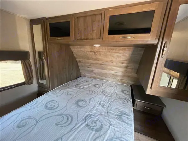 Cozy RV rental bedroom with a patterned mattress, wood cabinets, a side window, and a full-length mirror.. Coleman 2305QB 2018