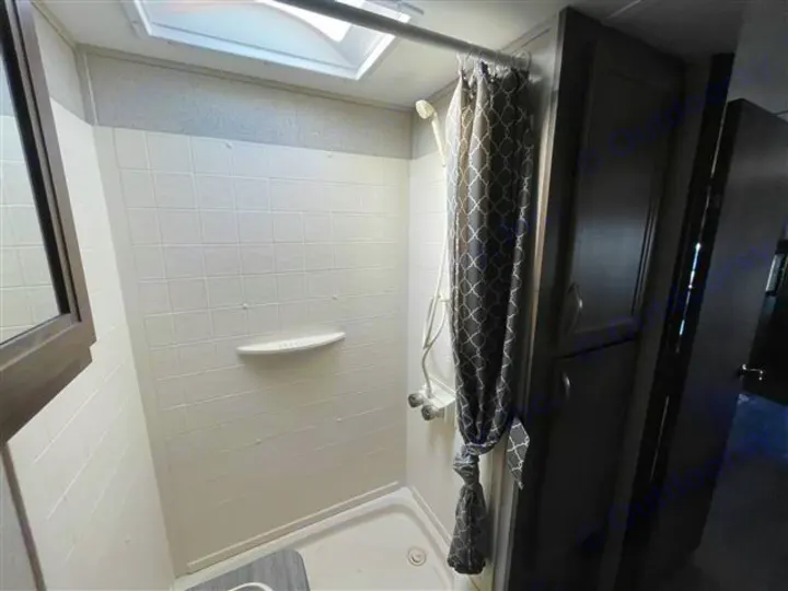 Compact white-tiled shower in an RV rental, featuring a grey patterned curtain, skylight, and small shelf.. Coleman 2305QB 2018