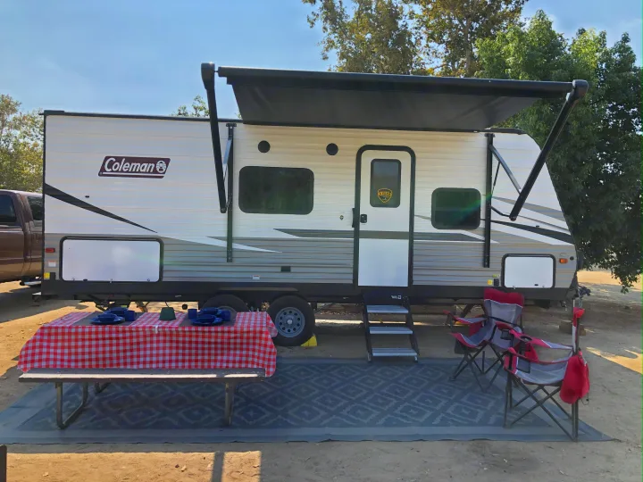 RV rental at a sun-drenched campsite, featuring a picnic table, awning, and outdoor chairs.. Dutchmen Coleman Lantern LT 2021
