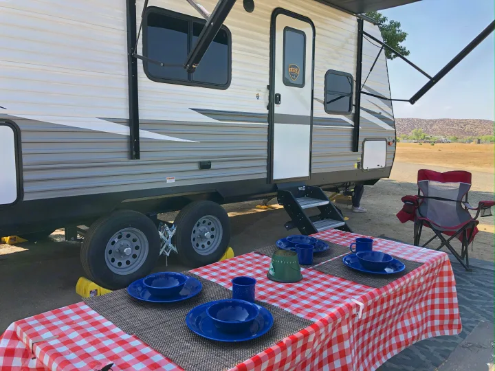This RV rental is set up for camping, featuring an extended awning, outdoor steps, and a picnic table with place settings.. Dutchmen Coleman Lantern LT 2021