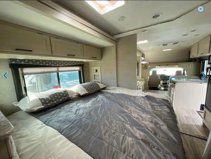 Spacious RV rental interior: Bedroom with gray comforter, flowing into the living area and cockpit.. Thor Freedom Elite 2023