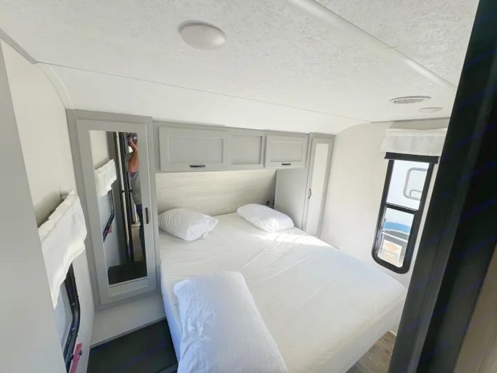 Inside an RV rental: a modern bedroom with white bedding, gray cabinets, dual mirrors, and ceiling AC vent.. Forest River Vibe 2021