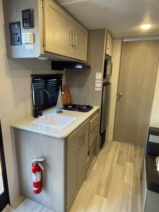Modern and compact kitchenette in an RV rental, with sink, stovetop, microwave, fridge, storage, and wall-mounted controls.. Keystone Rv company 1800bh 2024