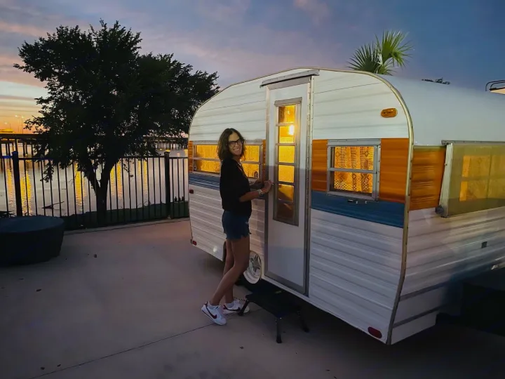 Experience the joy of camping! A happy woman with her colorful RV rental at sunset by the lake.. Play-Mor Other 1978