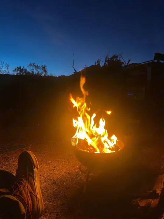 A warm campfire glows in the desert as a shoe rests nearby, complementing our RV rental experience at night.. Hiker MXL5x10 2022