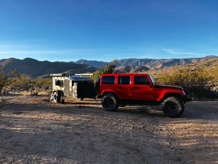 Red Jeep & rugged overland trailer parked in a sunny desert landscape with mountains. Explore with an off-road RV rental!. Hiker MXL5x10 2022