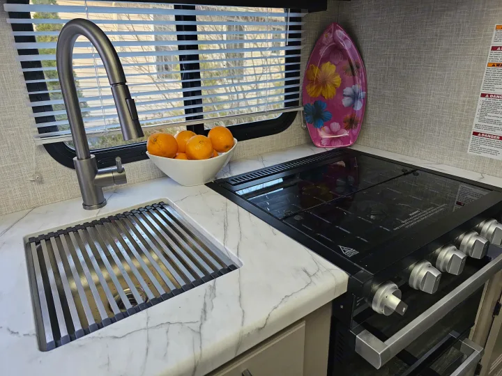 Modern RV rental kitchen with sink, flexible faucet, rolling drying rack, stove, and marble-look countertop.. Other Other 2024