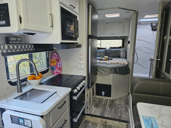 Inside a well-appointed RV rental, showing a kitchen with sink and stove, a bedroom area, and a refrigerator. Ideal for adventures.. Other Other 2024
