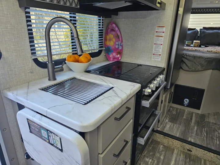 Compact RV rental kitchen features a sink, stove, countertop, and fold-out extension for efficient mobile living.. Other Other 2024