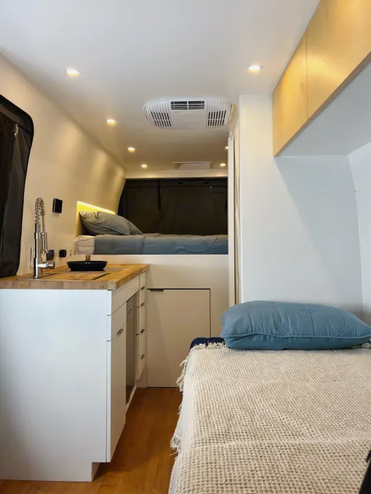 Modern RV rental interior with a compact kitchen, elevated bed, and additional sleeping area. Bright and functional design.. RAM Promaster 3500 extended wheel base 2023
