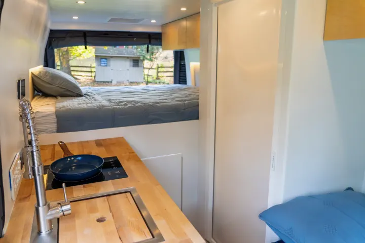 This RV rental's van conversion offers a compact kitchen and comfy elevated bed, ideal for tiny home on wheels travel.. RAM Promaster 3500 extended wheel base 2023