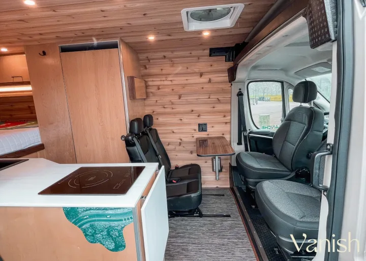 Detailed view of a modern RV rental interior, showcasing a compact kitchen, cedar walls, and versatile passenger seating.. Ram Promaster 2022