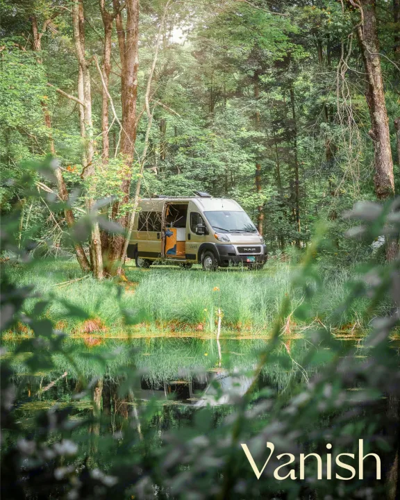 Explore nature with this tan camper van rv rental parked by a reflective pond in a tranquil forest.. Ram Promaster 2022