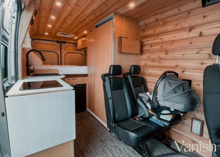 This RV rental interior features a cozy kitchen, bed, passenger seats, and a baby car seat, perfect for family vanlife.. Ram Promaster 2022