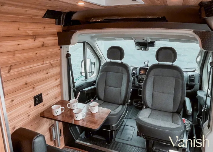 This RV rental offers a cozy camper van interior: wooden walls, swiveling front seats, and a small table for comfortable travel.. Ram Promaster 2022