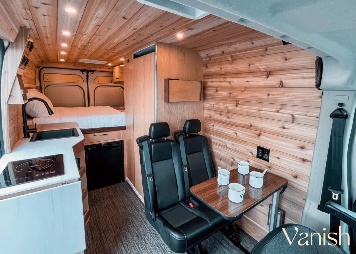 Explore this modern RV rental interior featuring a bed, kitchenette with sink & cooktop, and dining area. Comfort on the road!. Ram Promaster 2022