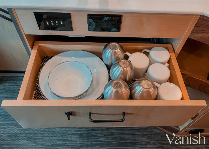 RV rental kitchen drawer open, revealing stacked plates, bowls, and metal cups. USB ports & power outlets above.. Ram Promaster 2022