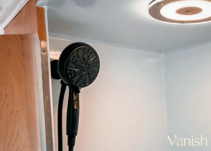 Inside an RV rental: a modern, compact shower stall with a black shower head and bright ceiling light, ideal for travel.. Ram Promaster 2022