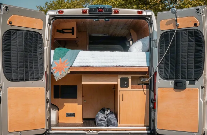 This RV rental reveals a cozy camper van interior with a bed, storage, and shower, perfect for mobile adventures.. Ram Promaster 2021
