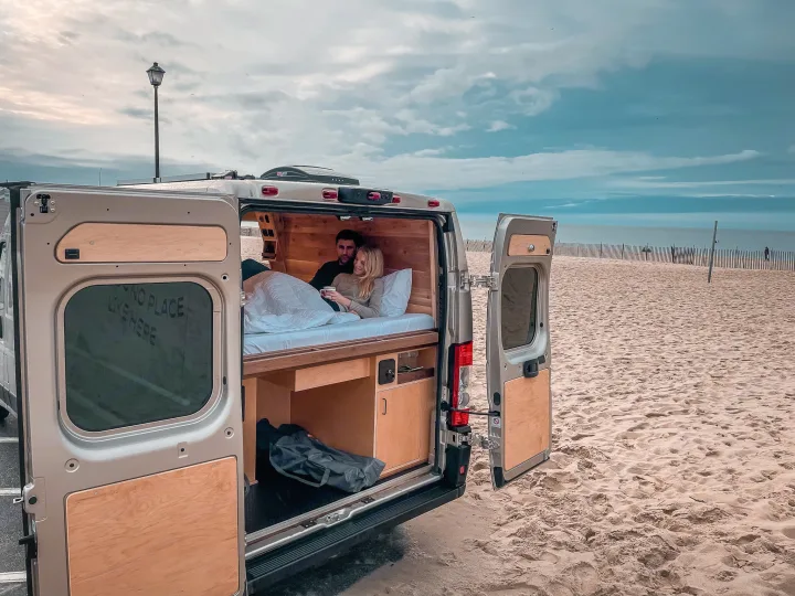 Relaxing beach getaway with an rv rental! A couple enjoys a cozy morning view from their custom van by the sea.. Ram Promaster 2021