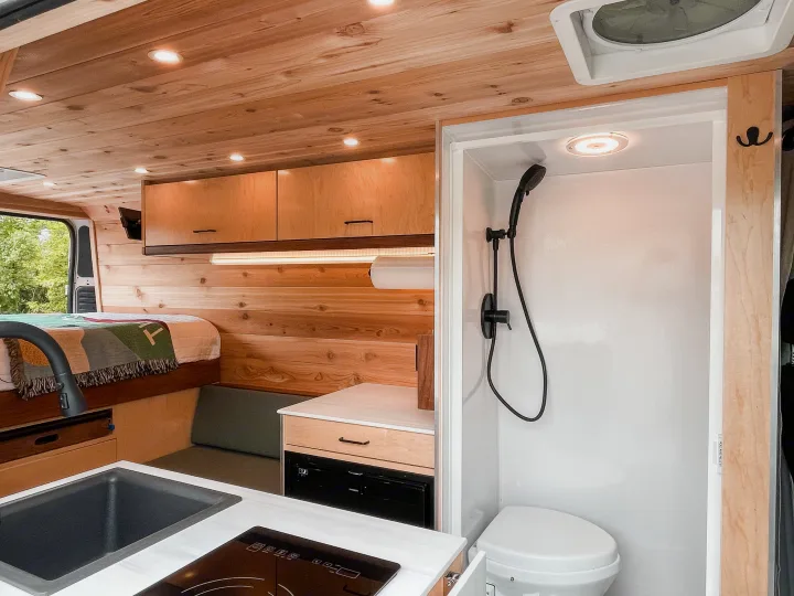Step inside this RV rental's cozy interior, featuring wood paneling, a comfy bed, functional kitchen, and compact wet bath.. Ram Promaster 2021