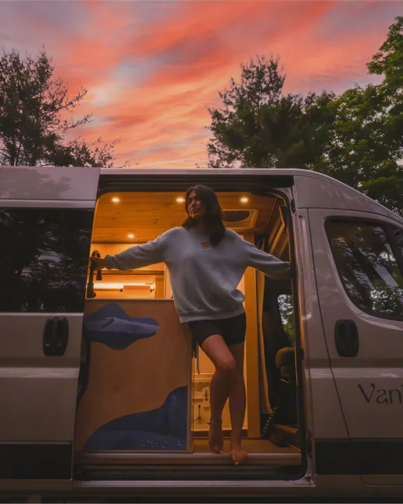 Woman stands in a modern rv rental camper van at a vibrant sunset. Experience van life and outdoor travel.. Ram Promaster 2021
