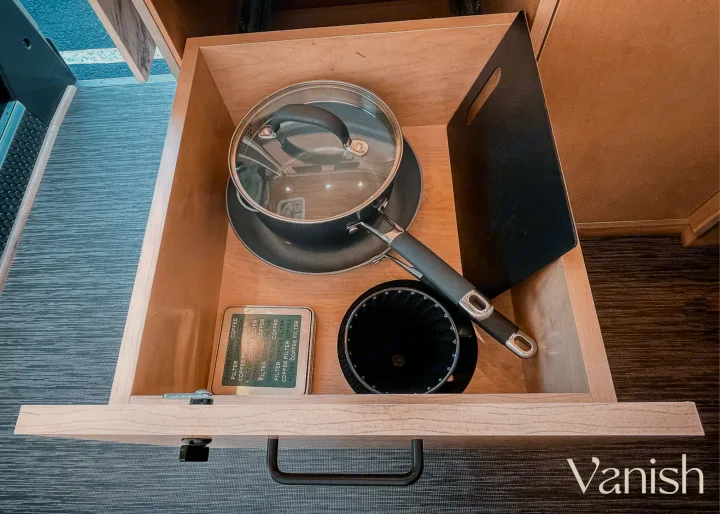 Open RV rental kitchen drawer revealing a pot, pour-over coffee dripper, and coffee filters. Essential compact travel setup.. Ram Promaster 2021