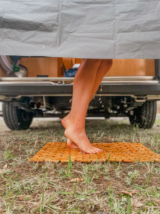 Enjoying a refreshing outdoor shower with an RV rental, feet on a wooden mat, surrounded by nature.. Ram Promaster 2021