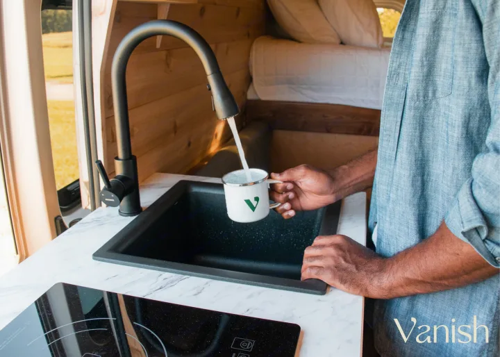 Man fills a mug in a cozy, wood-paneled RV rental kitchen. Modern amenities for your camper adventure.. Ram Promaster 2021