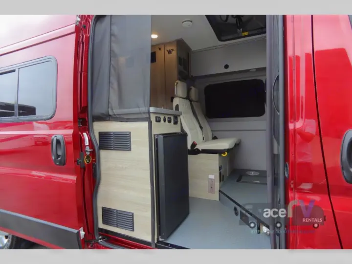 Red camper van interior with open side door revealing a compact kitchen, seating, and mesh screen. An ideal rv rental.. Winnebago Solis 2021