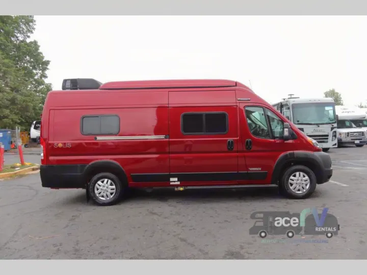 A shiny red Winnebago Solis camper van for rv rental, parked on an asphalt lot with other RVs in the background.. Winnebago Solis 2021