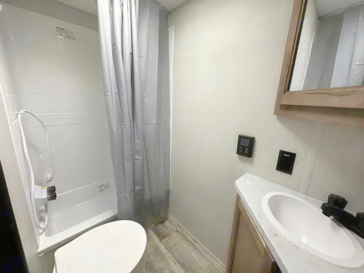 Compact RV rental bathroom features a tub/shower combo, toilet, and vanity with sink and mirror.. Forest River 19' Bunkhouse with Slide 2024