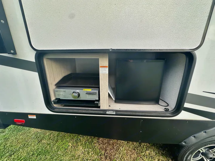 RV rental with convenient outdoor kitchen, featuring a GREYSTONE griddle and mini-fridge in an exterior compartment.. East to West Alta 2022
