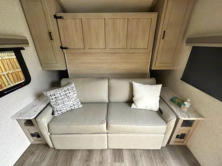 RV rental interior: A light sofa under a hidden wall bed, flanked by side tables with outlets. Compact comfort.. East to West Alta 2022