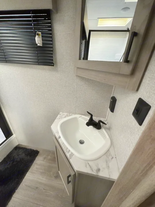 Inside an RV rental: a compact bathroom featuring a white sink, black faucet, mirror, blinds, and wood-look floor.. East to West Alta 2022
