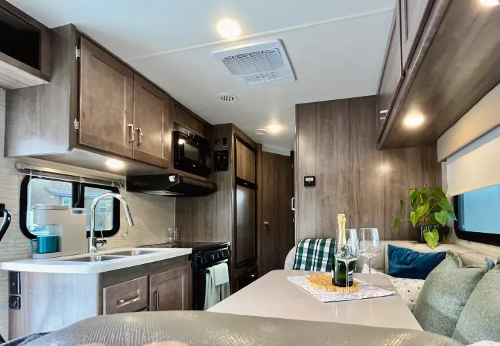 Inside a stylish rv rental: a full kitchen with microwave, stove, sink, and dining area featuring a celebratory champagne setting.. Winnebago Minnie Winnie 2022