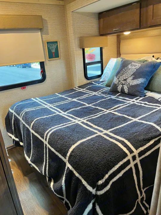 Cozy RV rental bedroom featuring a bed with a dark plaid blanket, owl pillow, and a "LET'S SLEEP UNDER THE STARS" framed art.. Winnebago Minnie Winnie 2022