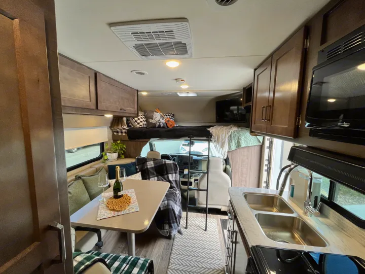 This RV rental interior features a functional kitchenette, inviting dining area, and a cozy overhead bunk bed, perfect for travel.. Winnebago Minnie Winnie 2022
