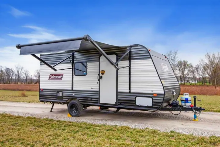 A Coleman travel trailer, perfect for rv rental, parked on a gravel path with its awning extended for outdoor camping enjoyment.. Coleman 17B 2024