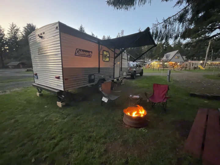 RV rental at a cozy campground, featuring a Coleman travel trailer, fire pit, and chairs under the evening sky.. Coleman 17B 2024