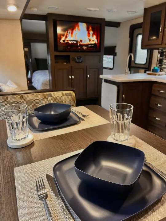 Interior of an RV rental featuring a cozy dining table set for two, a functional kitchen, and a glimpse of the bedroom beyond.. Forest River Wildwood X-Lite 2019