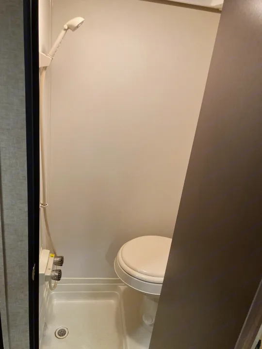 An RV rental's compact wet bath features a toilet next to a shower area with a handheld showerhead and drain.. Forest River Cherokee Wolf Pack Toy Hauler 2017