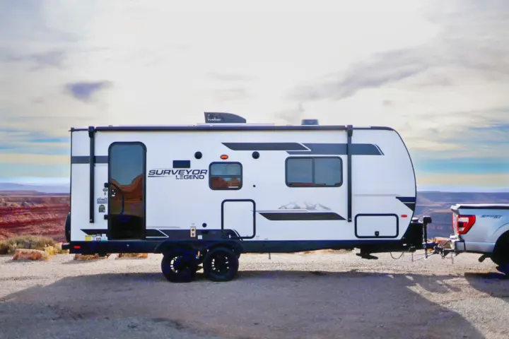 White Surveyor Legend travel trailer, perfect for your next rv rental adventure, hitched to a truck with a scenic canyon view.. Forest River Surveyor Legend 202RBLE 2024