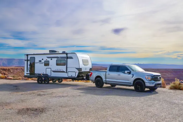 Silver Ford F-150 truck tows a Surveyor Legend RV on gravel, at a scenic desert overlook, ideal for an RV rental.. Forest River Surveyor Legend 202RBLE 2024