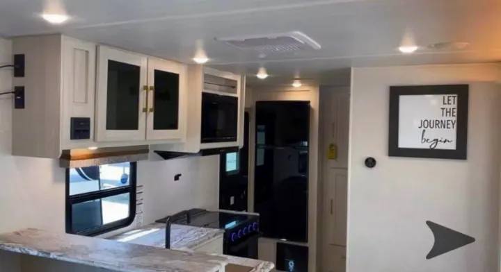 Modern RV rental kitchen with light cabinets, microwave, fridge, and "LET THE JOURNEY begin" wall art. Ready for travel!. Forest River Surveyor Legend 202RBLE 2024