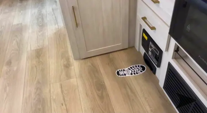 Bright RV rental interior showing light wood flooring, cabinet, control panel, and a black-and-white footprint decal.. Forest River Surveyor Legend 202RBLE 2024